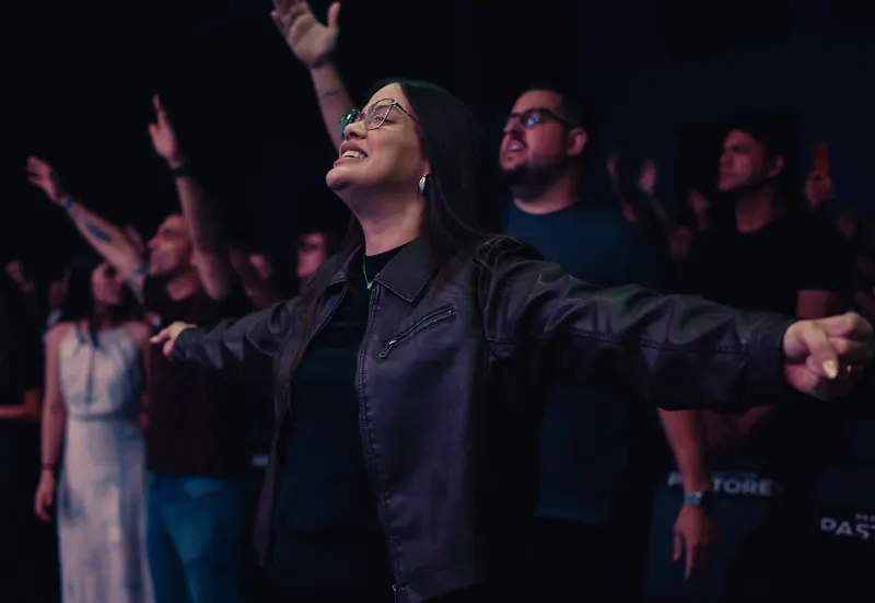 Nathália Carvalho de braços abertos em adoração, em meio à igreja