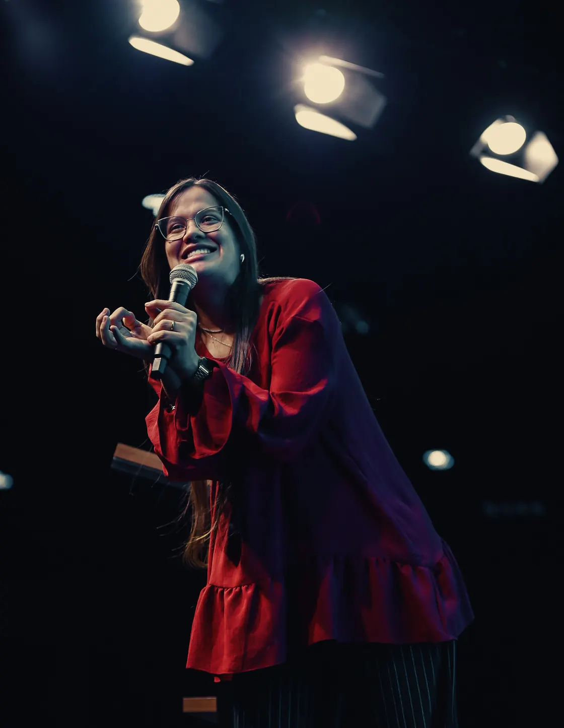 Nathália Carvalho sorri no palco, com o microfone na mão, sob as luzes